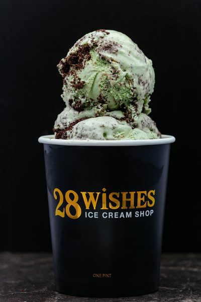 Two scoops of pale green ice cream with dark chocolate chunks in a black 28 Wishes cup